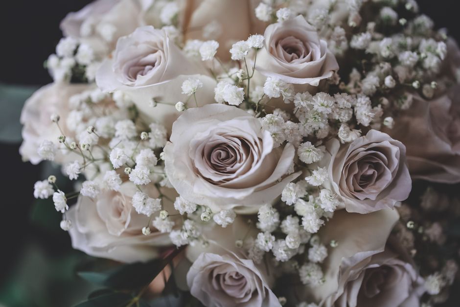A close-up of a floral arrangement consisting of cream-colored roses with soft, velvety petals, accented by delicate sprigs of white baby's breath with tiny clustered blooms. The roses are arranged in