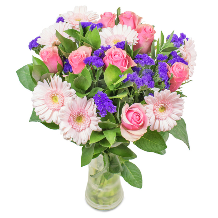 This vibrant floral arrangement, expertly curated and set in a clear glass vase, beckons from a pristine white backdrop-mirroring the freshness seen each week at Stevenage's bustling market stalls. At its heart, about 7 to 9 medium pink roses display a mix of tightly furled and slightly open petals, their classic spiral forms exuding a timeless appeal familiar to Stevenage's cherished gardens. Accompanying these, 5 to 7 soft pink gerbera daisies with wide, round faces and creamy centers add visual joy, reminiscent of early summer picnics at King George Recreation Ground. Bright, lively clusters of deep purple statice are interspersed for texture and colour depth, bringing a sense of movement and surprise, not unlike discovering wildflowers along the town's green corridors. Lush, deep green leaves provide the base, amplifying freshness and abundance and suggesting a recent handpick from a garden off Broadwater Crescent. The clear vase reveals stems and fresh water, reinforcing the artistry and care so often found in a local Stevenage flower delivery. Altogether, this bouquet-composed of roses, gerberas, and vibrant purple fillers-makes a joyful birthday gift, a heartfelt Mother's Day offering, or an elegant office accent near Gunnels Wood, filling every space with celebration and sincere affection.