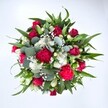 Viewed from directly above against a clean white background, this luxurious bouquet forms a perfect, rounded canopy of colour and texture, as if you are peering down into the heart of a garden in full bloom. Deep crimson red roses sit at the centre, some still in tight bud and others just beginning to unfurl their velvety petals, suggesting quiet romance and thoughtful affection. Around them, rich fuchsia and ruby red carnations puff out in ruffled layers, their fringed edges catching the light and adding a festive liveliness to the composition. Nestled between these bold tones are clusters of crisp white spray chrysanthemums, their daisy-like faces glowing softly, creating sparkling highlights that keep the arrangement bright and fresh. Tiny white gypsophila, or baby's breath, threads through every gap like a mist of delicate stars, softening the transitions between flowers and giving the bouquet a dreamy, cloudlike finish. Supporting this tapestry of blooms is a ring of lush greenery: pointed, glossy dark green leaves, likely from lilies or alstroemeria, provide structure and a sense of movement as they arc outward, while silvery-green eucalyptus leaves with their rounded shapes weave a cooler, contemporary note into the design. You can almost imagine the gentle, herbal scent mingling with the sweetness of the roses. The image feels like natural daylight in a Stevenage studio, the kind of bouquet a local florist might set out ready for same-day delivery to homes near Fairlands Valley Park or along Bedwell roads. It radiates joy and heartfelt celebration, perfect for birthdays, anniversaries, or simply sending a warm, uplifting message to someone special in town.