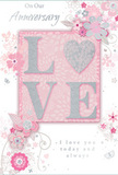Softly romantic anniversary card that blends pastel pinks and silvery greys to create a feeling of cherished intimacy, reminiscent of a quiet dinner at home in Stevenage's Old Town. At the centre, the word LOVE is written in elegant, slightly raised letters, the surface dusted with fine glitter so that it shimmers delicately when it catches the light. The letter O is replaced by a small, silver-toned heart, richly textured with glitter that gives it a three-dimensional, jewel-like presence. Surrounding this focal motif, a gentle arrangement of blooms in blush, mauve, and soft rose pink appears to unfurl across the card. The flowers have a watercolor softness, with edges that seem to fade gently into the background, while slender stems, curving tendrils, and scattered petals convey a sense of light motion, as if stirred by a soft spring breeze off Fairlands Valley Park's lakes. Tiny flourishes-subtle butterflies, graceful swirls, and decorative leaves-add a hint of playfulness and romance without detracting from the card's refined calm. The phrases On Our Anniversary and I love you today and always are written in a delicate script that feels intimate and sincere, like handwriting in a cherished love letter. The overall composition exudes a lovely sense of occasion-neither loud nor showy, but quietly profound, perfect for a couple who value shared moments and gentle gestures. Paired with fresh flowers delivered across Stevenage, this card becomes a tender token of a journey shared, soft as a whisper yet filled with heartfelt emotion.